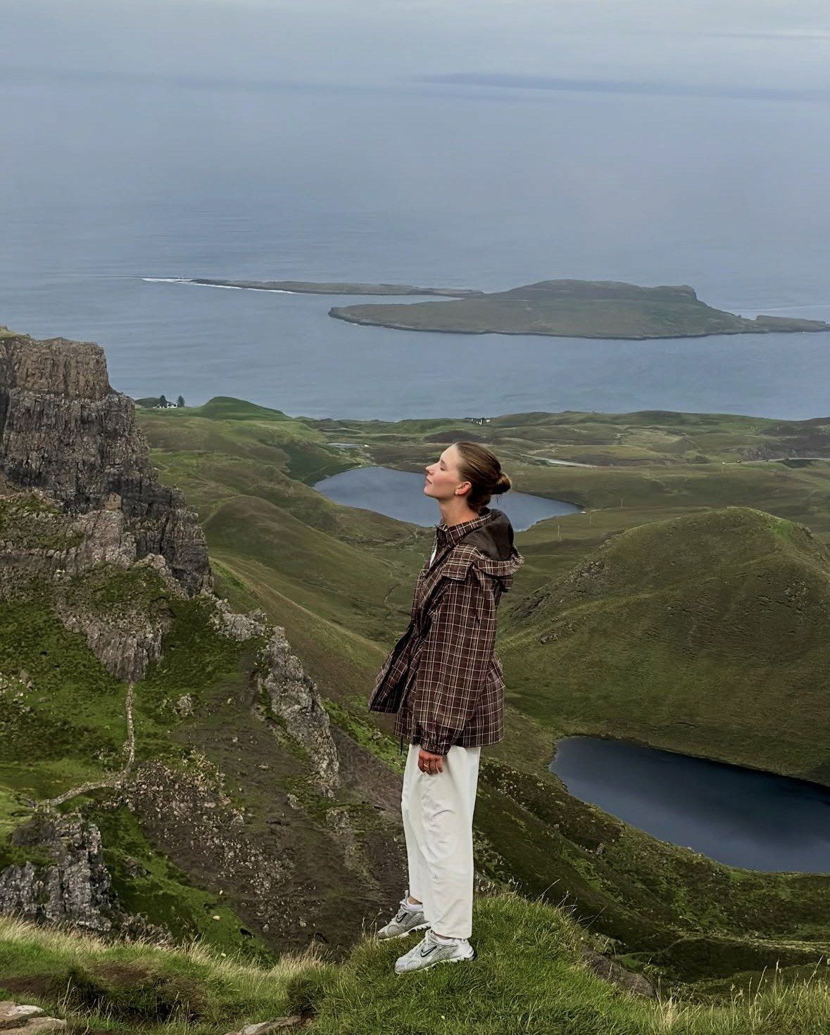 Donna in piedi sulla scogliera guarda l'isolotto e il mare di Skye