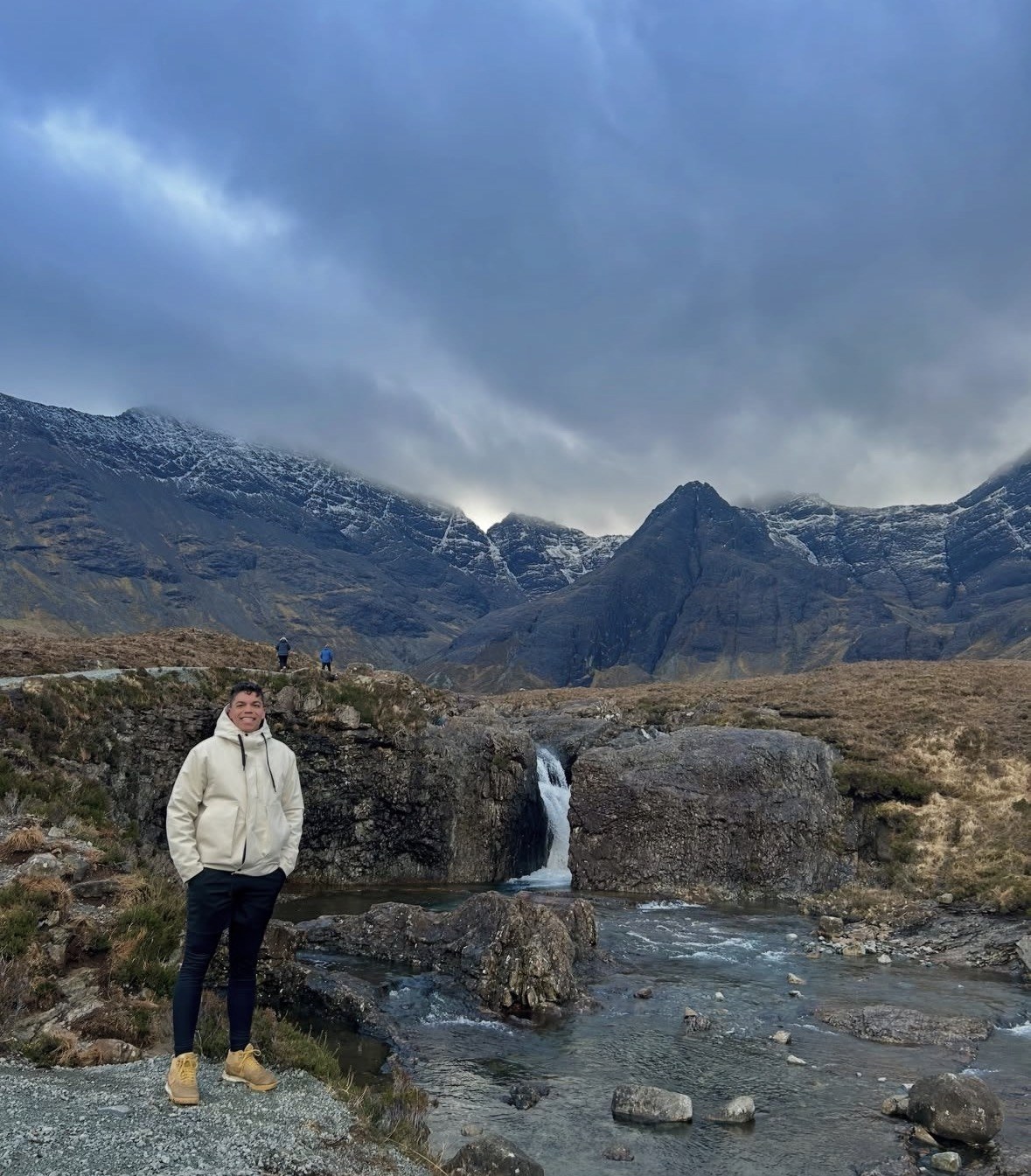 Viaggiatore accanto a una cascata delle Fairy Pools, Cuillin coperte di nuvole