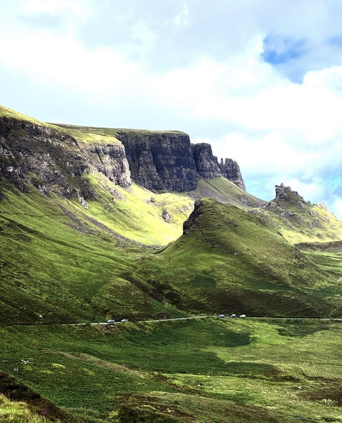 Strada ai piedi della scarpata del Quiraing, pendii verdi illuminati dal sole estivo